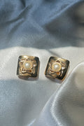 Pair of gold earrings with pearl centers on a light blue fabric background