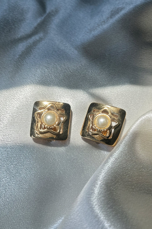 Pair of gold earrings with pearl centers on a light blue fabric background